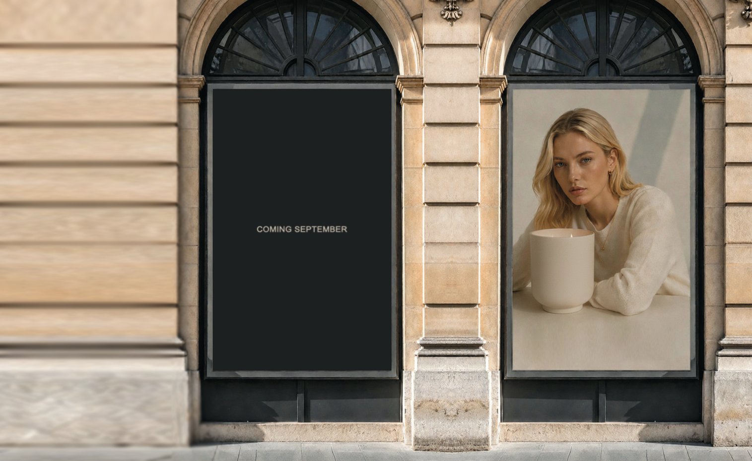 A storefront facade with two arched display windows. The left window is black with the text 'COMING SEPTEMBER' in white. 